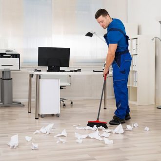 Full length of male janitor cleaning floor with broom in office