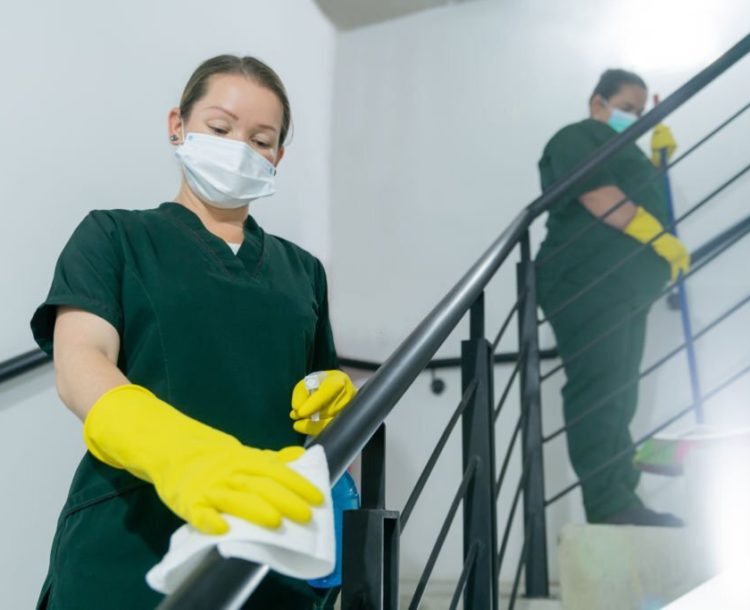 Team of Latin American cleaners cleaning the handrail of the stairs at a building during the COVID-19 pandemic