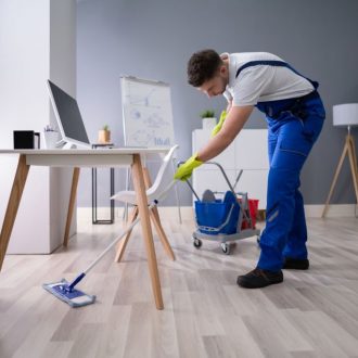 Happy Young Man Cleaning The Floor With Mop In Modern Office